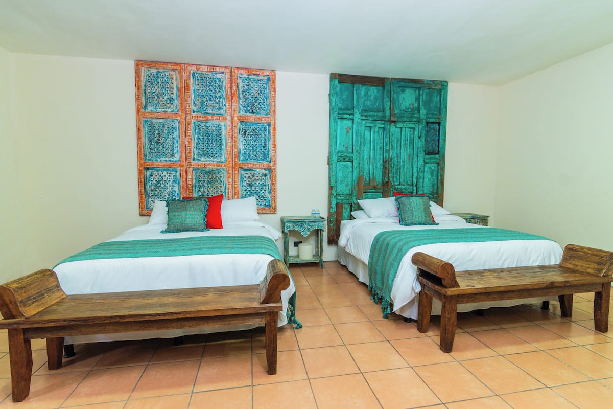 A room with two beds, a wooden bench, a patterned wall, and a teal door.