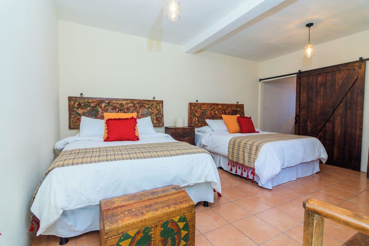 Two single beds with headboards, a wooden chest, and a sliding barn door in a room with tiled flooring.