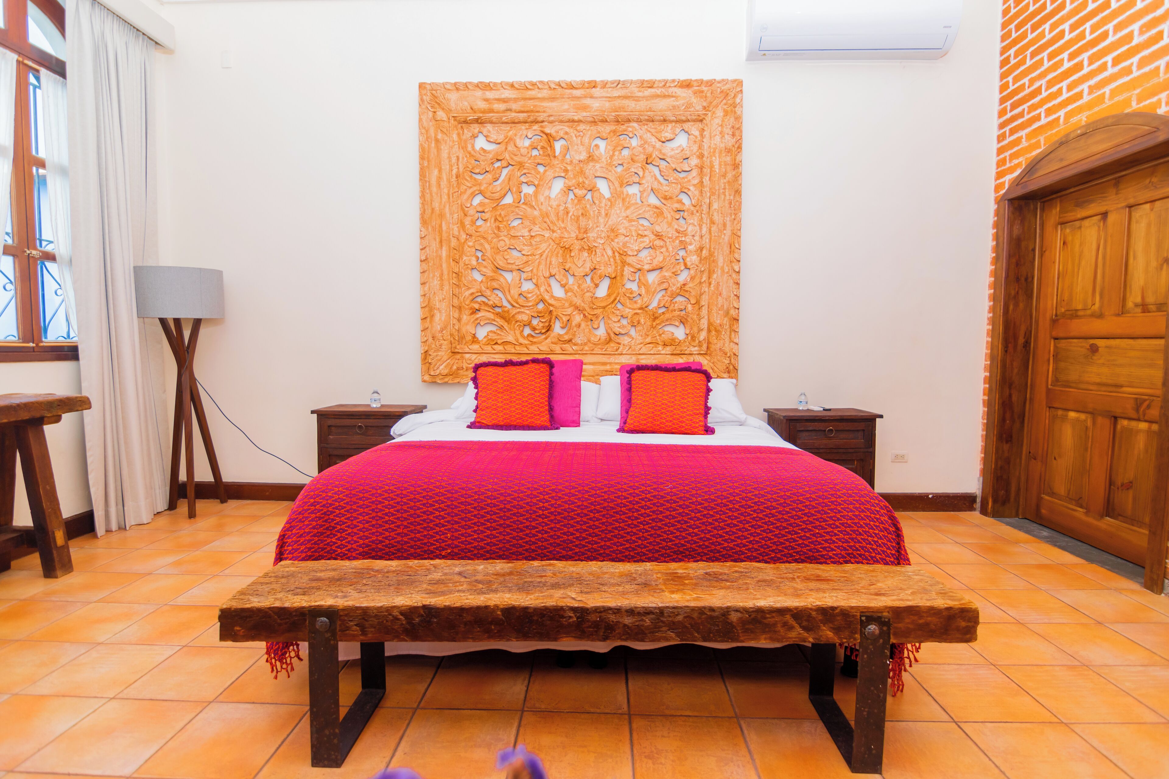 A bed with a wooden headboard, two bedside tables, a bench, and a window with curtains.