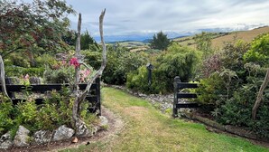 A garden pathway leading to a gate, surrounded by lush greenery and a view of rolling hills. - Greenwood Homestead (Tarara)