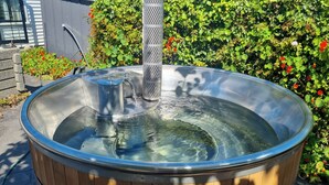A hot tub with a metal structure in the center, surrounded by greenery and a stone wall. - Greenwood Homestead (Tarara)
