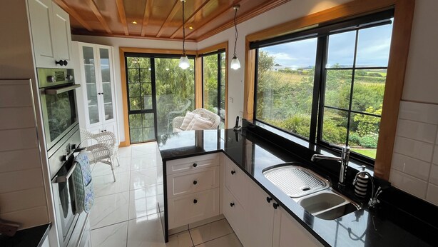A modern kitchen with a large window, white cabinets, and a black countertop. - Greenwood Homestead (Tarara)