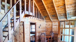L’intérieur d’un chalet en bois, avec un escalier, un coin repas et une grande fenêtre.