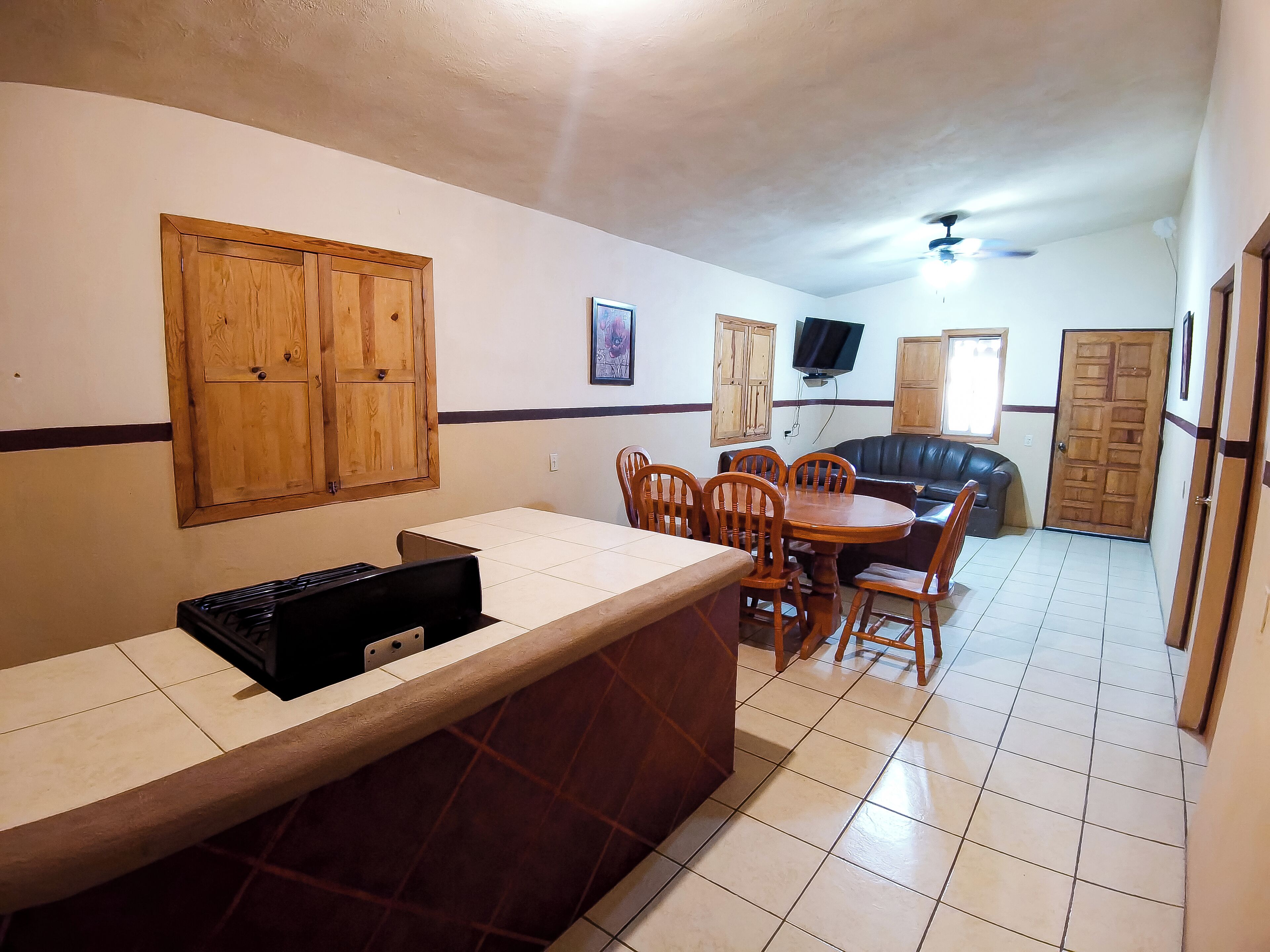 A kitchen with a dining area, wooden cabinets, a television, and a ceiling fan.