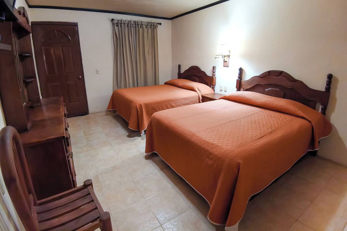 Una habitació amb dos llits, un escriptori de fusta, una cadira, una porta i una cortina.
