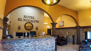 Un espace d’accueil doté d’un comptoir en pierre, d’un grand lustre et d’une enseigne indiquant « HÔTEL EL NOGALITO ».