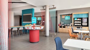 A modern cafe with a central island serving fresh fruits and pastries, a seating area with tables and chairs, and a coffee machine station.