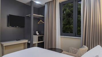 A hotel room with a bed, a desk with a flat-screen TV, a kitchenette, and a window with curtains.