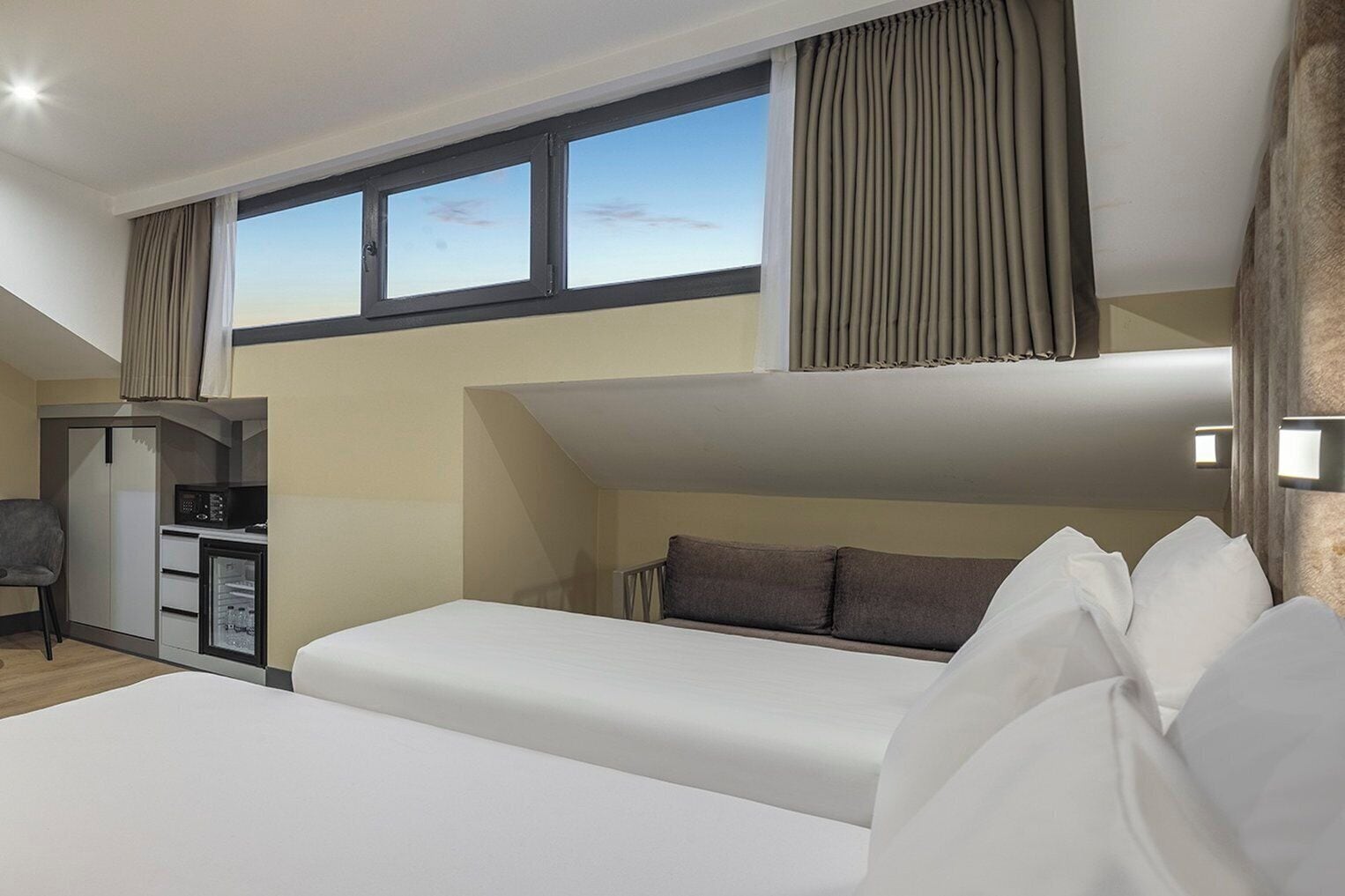 A modern hotel room with a bunk bed, a desk with a computer, and a view of the sky through the window.
