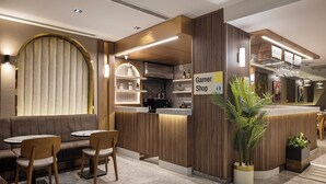 A modern interior with a wooden reception desk, seating area, and a kitchen visible in the background. - Garner Hotel Istanbul - Airport Arnavutkoy by IHG (Arnavutköy)