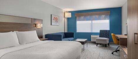 A hotel room with a large bed, a desk, a chair, and a small table.