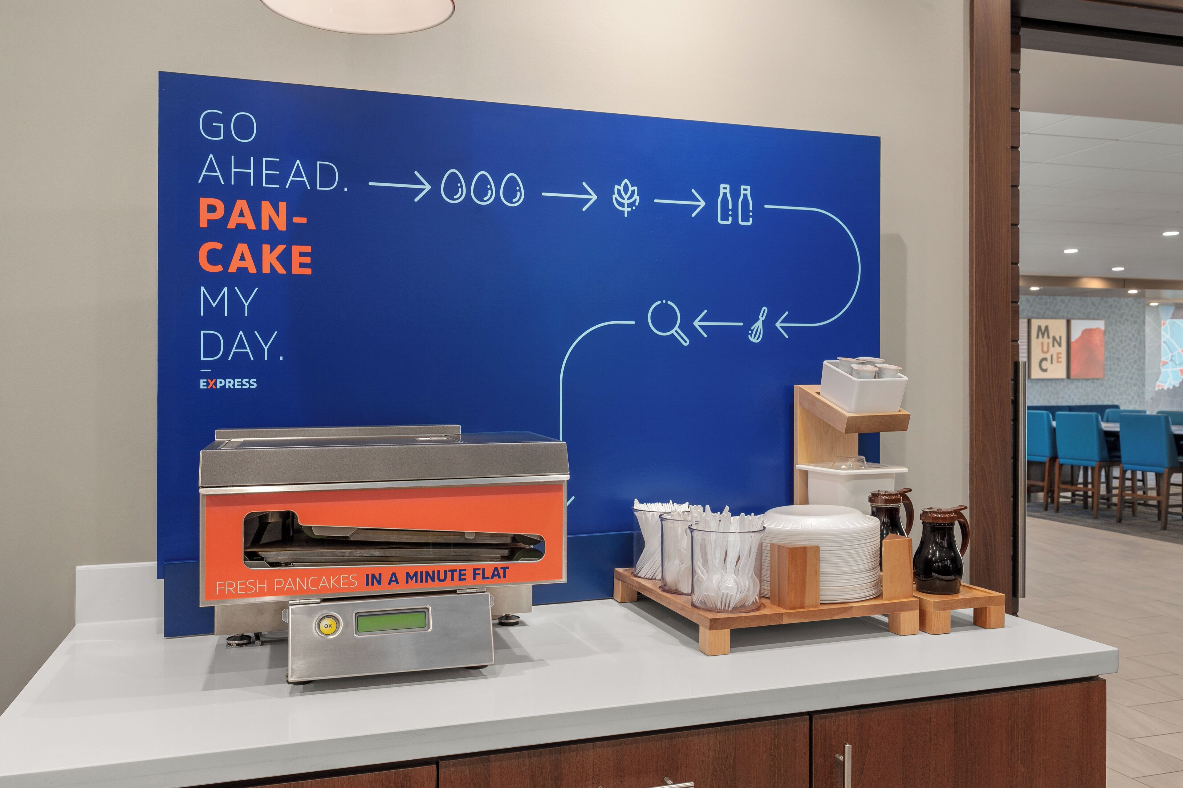 En morgenmadsstation med et skilt der står 'GO AHEAD. PANCAKE MY DAY.' og en flad pande til pandekager.