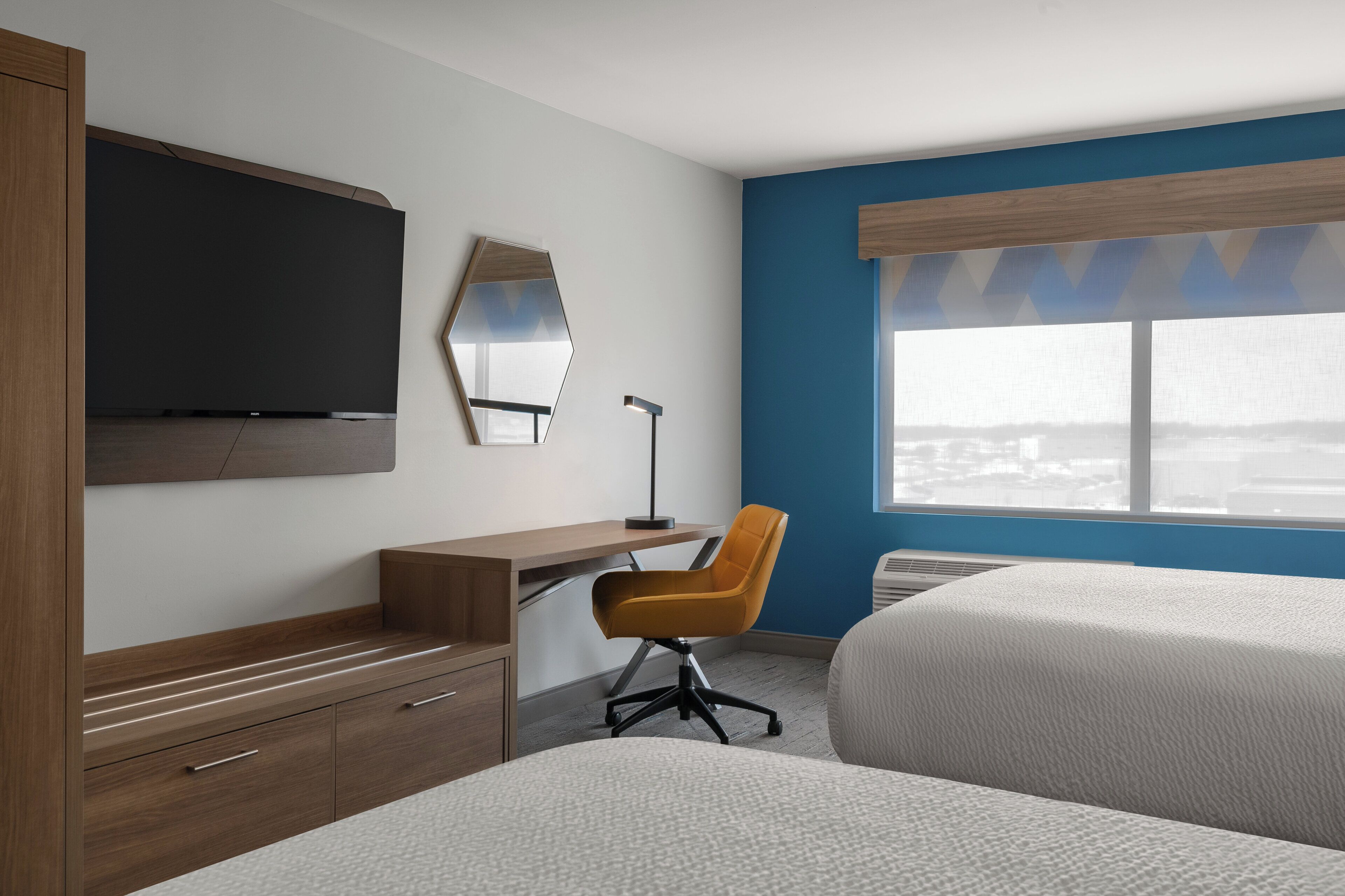 A hotel room with a bed, a desk, a chair, a TV, and a window with a view.