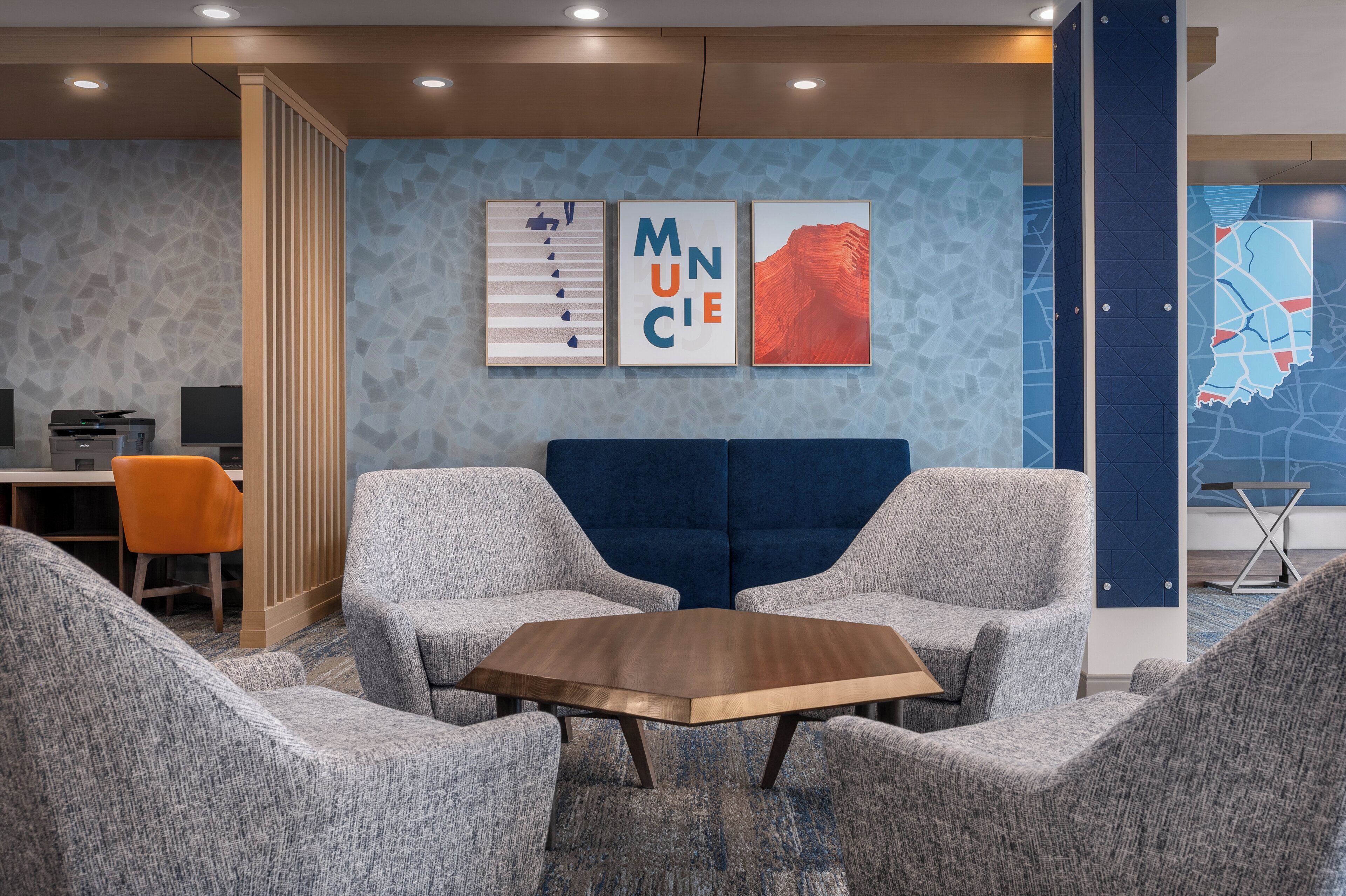 A modern lounge area with a wooden table, grey upholstered chairs, a blue sofa, and a map on the wall.