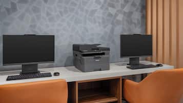 Un'area lavoro con due monitor, una stampante e una tastiera su una scrivania bianca.