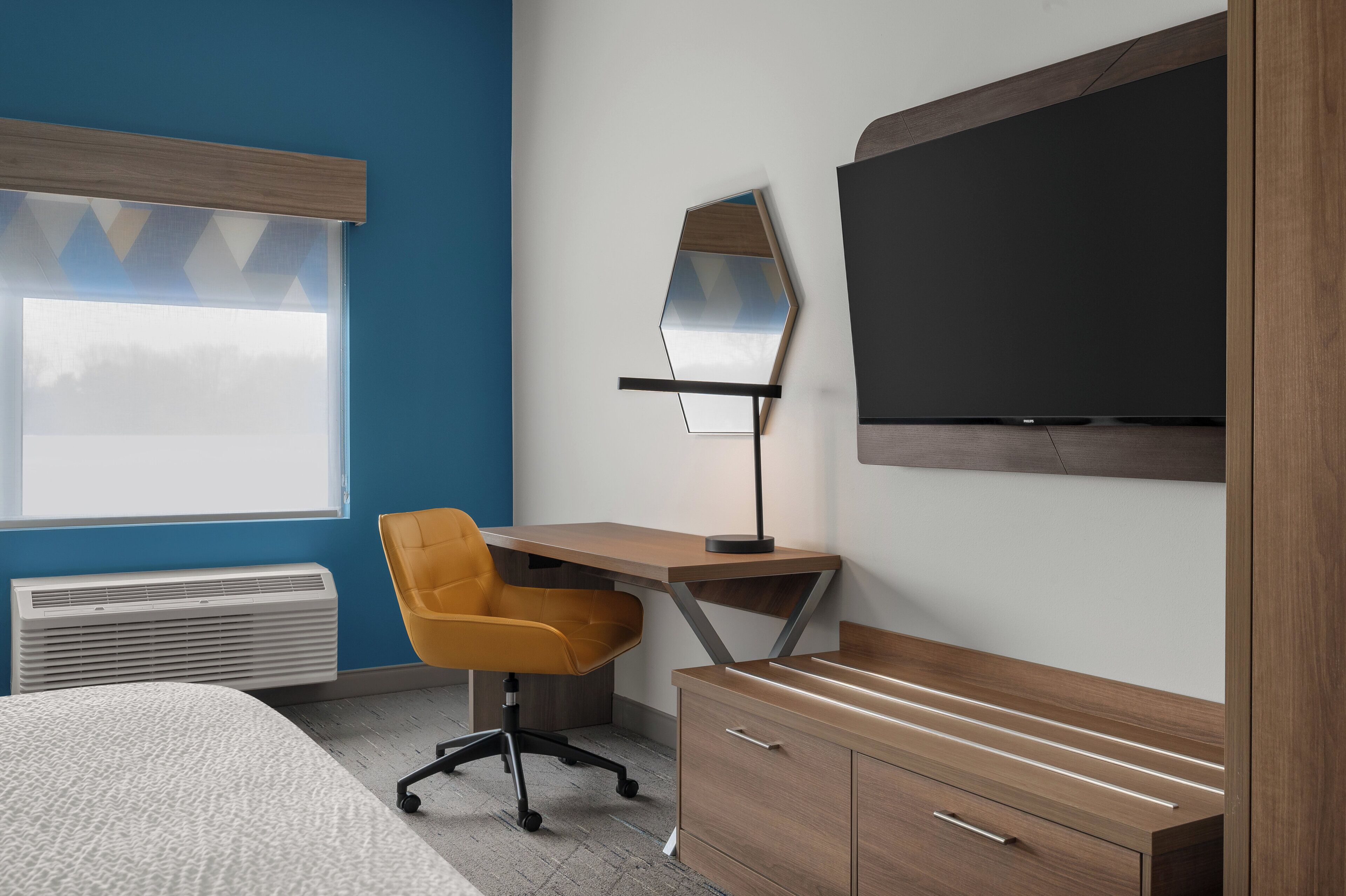 A modern room with a bed, a desk with a chair, a TV, and a heater.