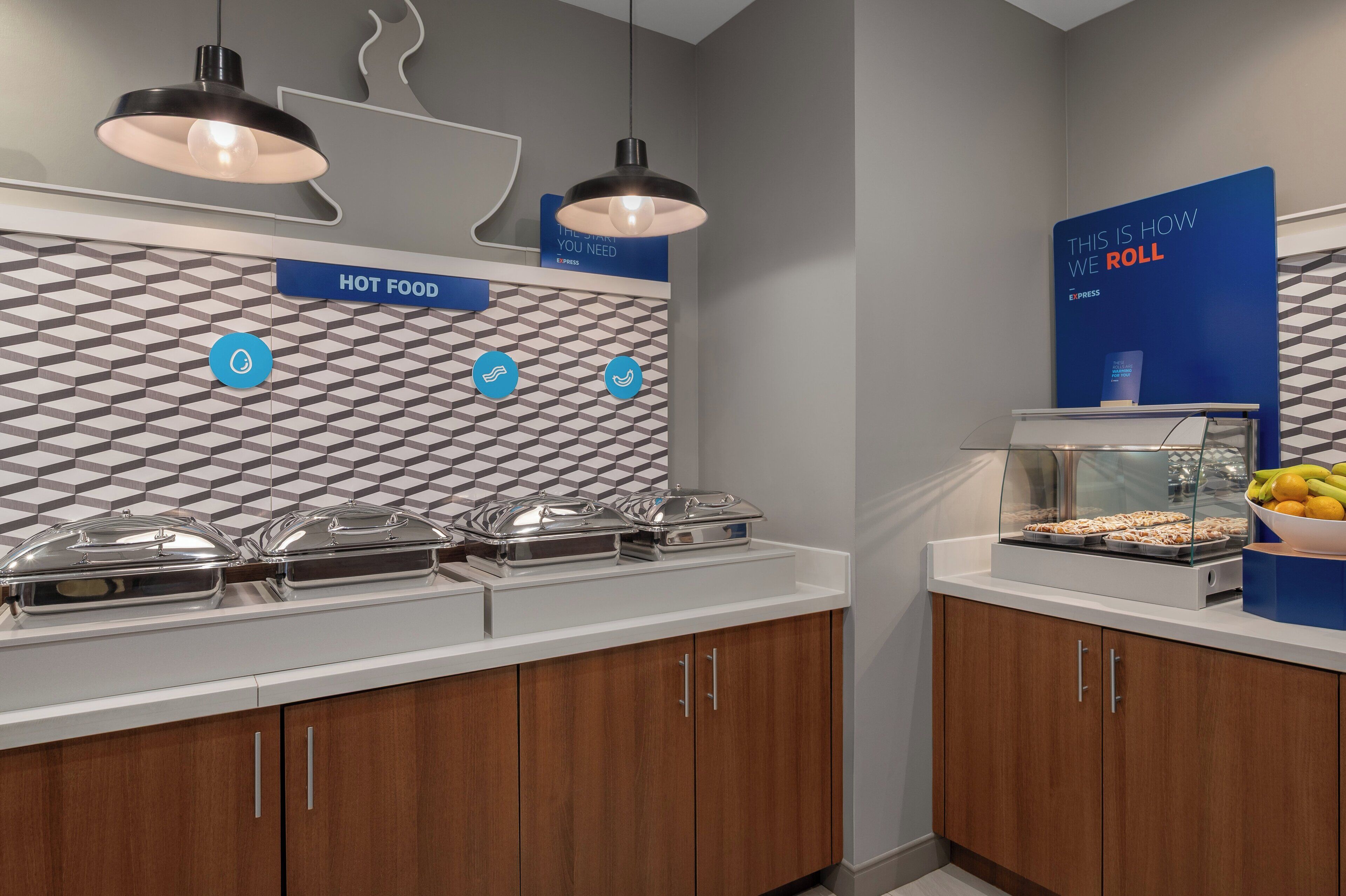 A buffet area with hot food options, a sign indicating the food is hot, and a blue sign with the text 'THIS IS HOW WE ROLL'.