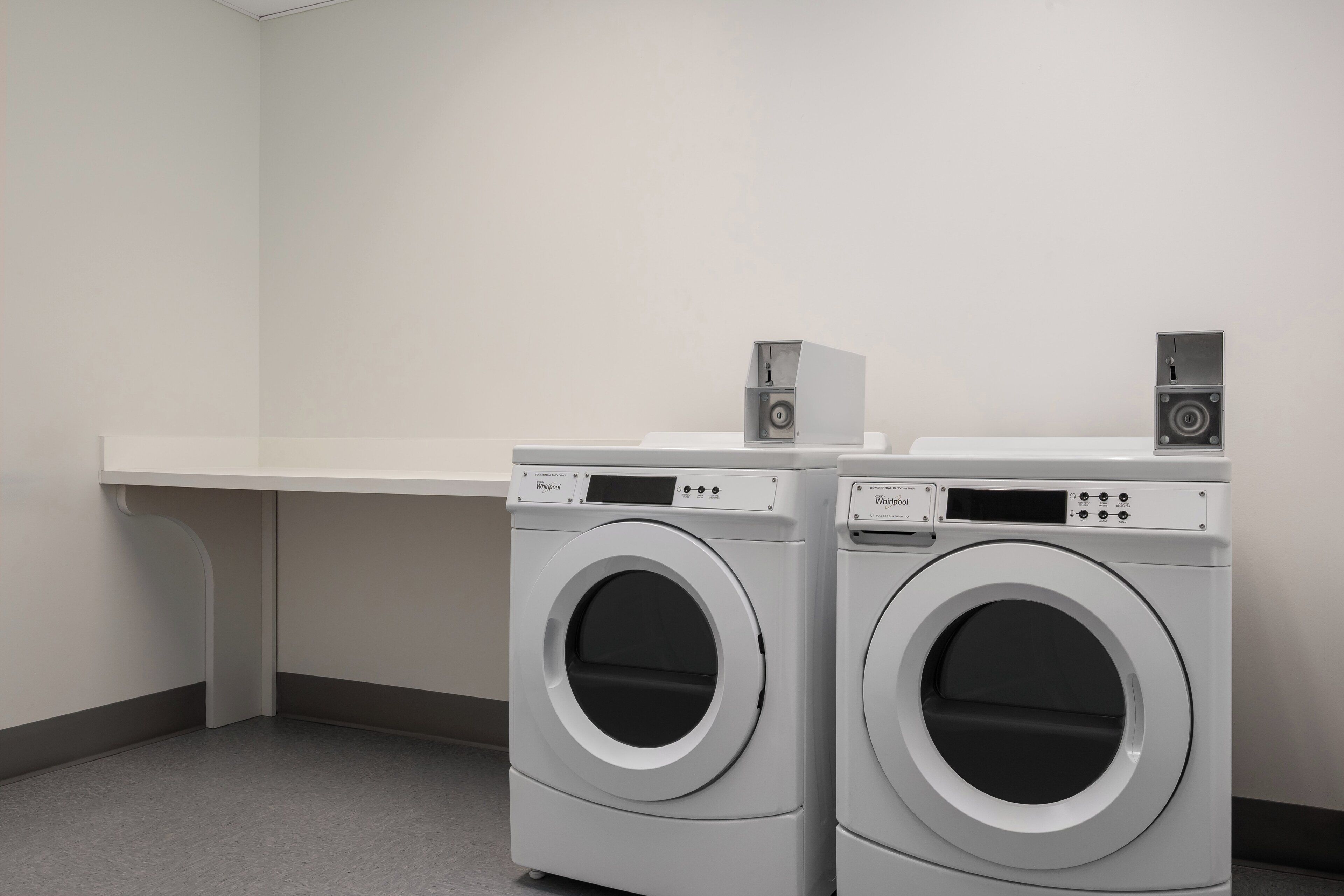 Two front-loading washing machines in a laundry room with a white countertop and a white wall.