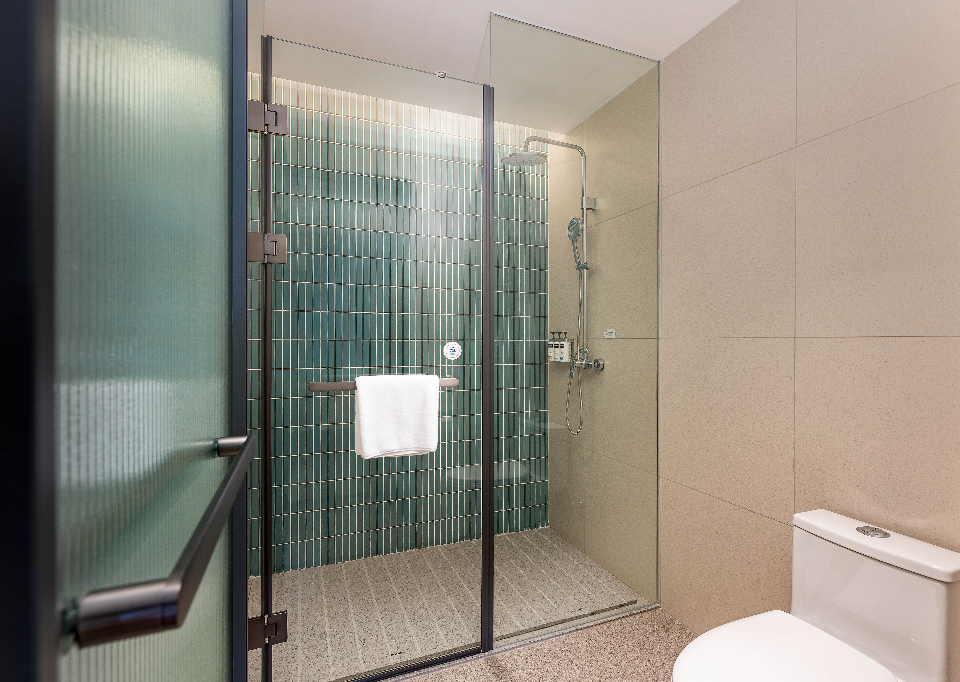 A glass-enclosed shower with a towel hanging on a rack, a toilet, and a tiled wall.