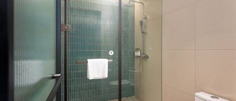 A glass-enclosed shower with a towel hanging on a rack, a toilet, and a tiled wall.