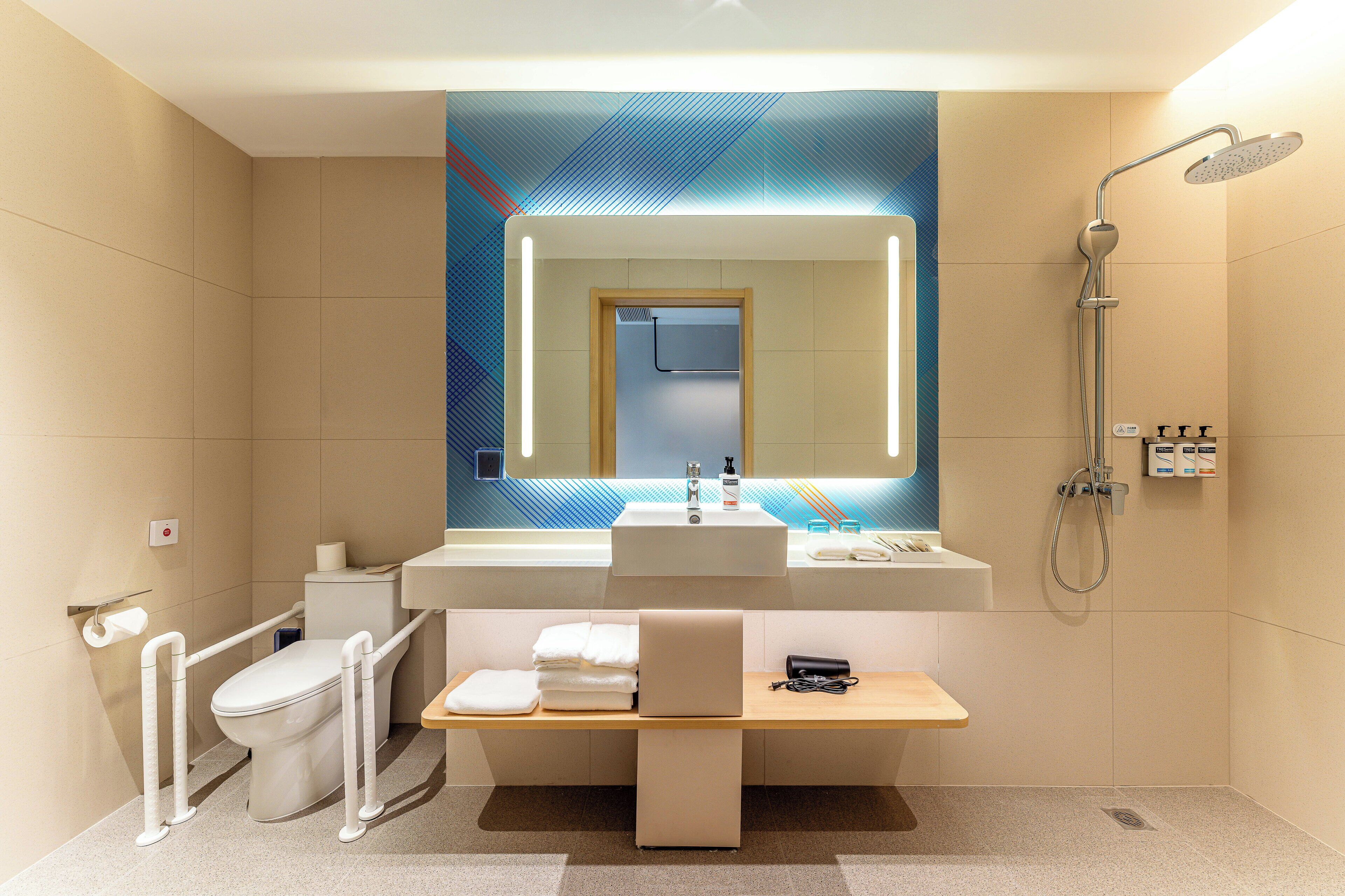 A modern bathroom with a large mirror, a shower, a toilet, and a vanity with a sink.