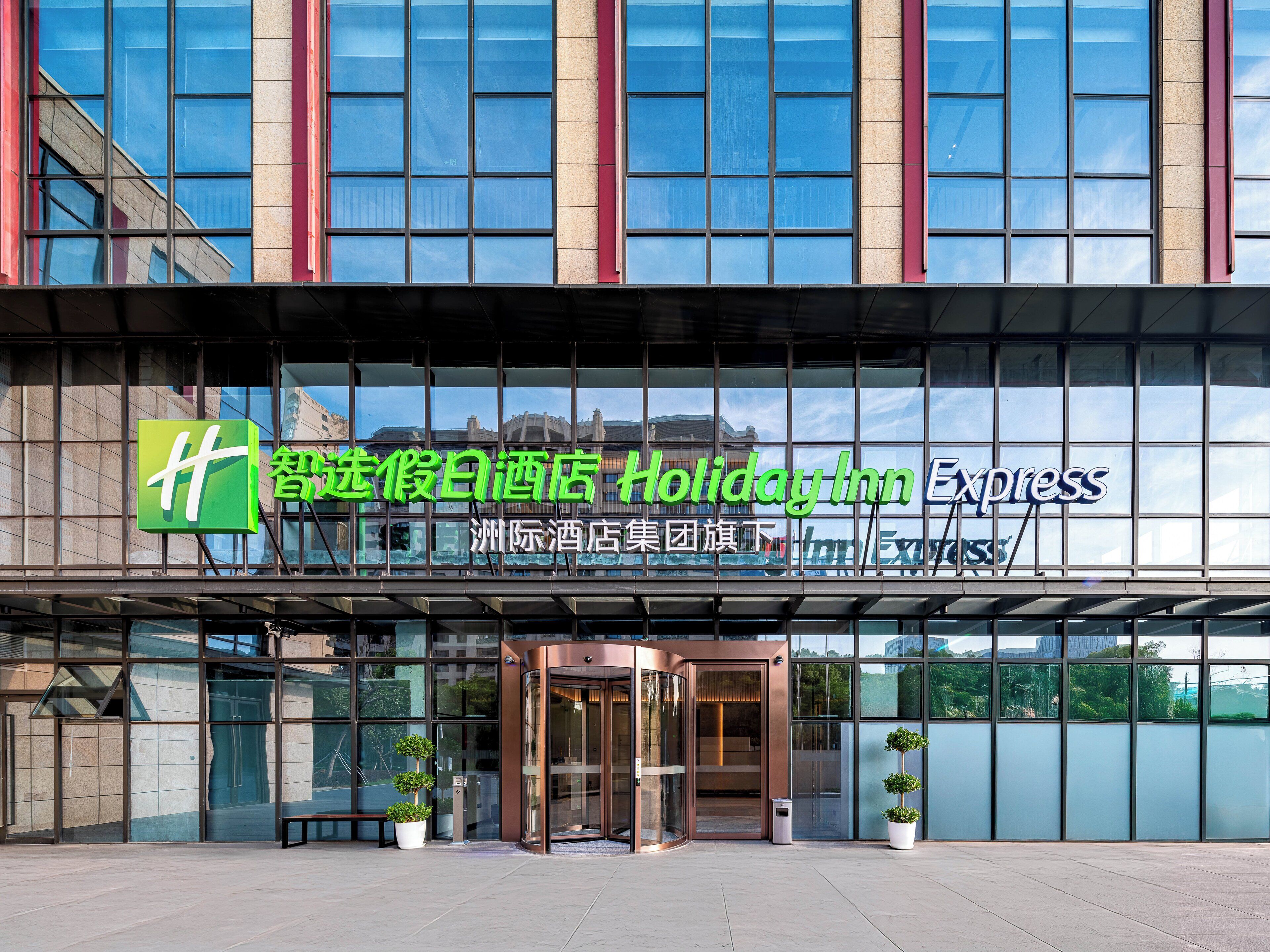 Der Eingang eines Holiday Inn Express Hotels mit Glasfassade, großen Fenstern und einer grün-weißen Beschilderung.