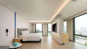 A modern hotel room with a large bed, a TV, a desk, and a view of the city. - Holiday Inn Express Kunshan Yushan by IHG (Suzhou)