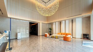 Een moderne lobby met een receptiebalie, zithoek en een decoratieve verlichtingsarmatuur.