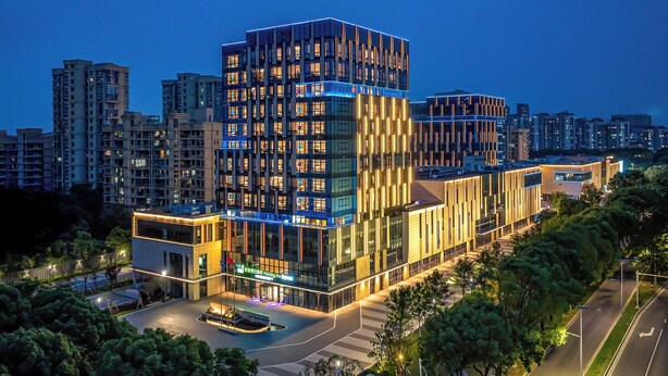 Een modern hotel met een opvallende glazen gevel, meerdere verdiepingen en een goed verlichte entree.