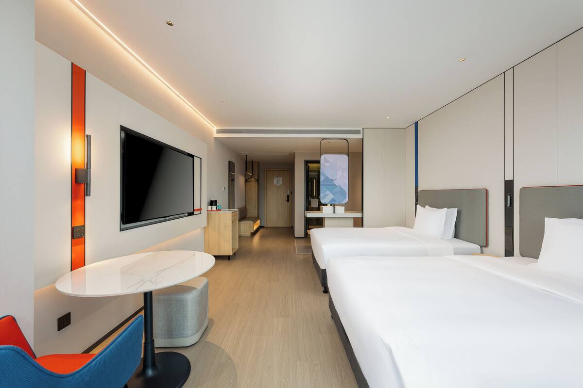 Una habitación de hotel moderna con dos camas, televisión, una mesita y una zona de estar.