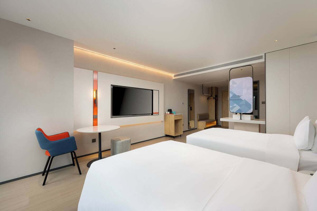 Una habitación de hotel con dos camas, televisión, escritorio y una silla.