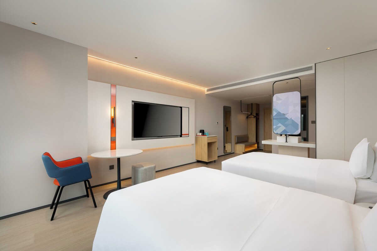 Una habitación de hotel con dos camas, televisión, escritorio y una silla.