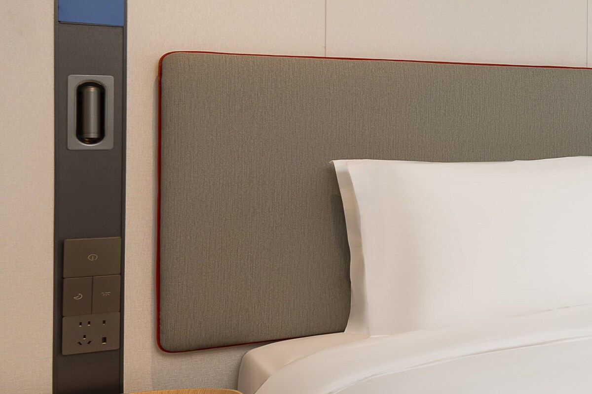 Habitación de hotel con una cama bien tendida, un panel de control en la pared y un cabecero con textura.