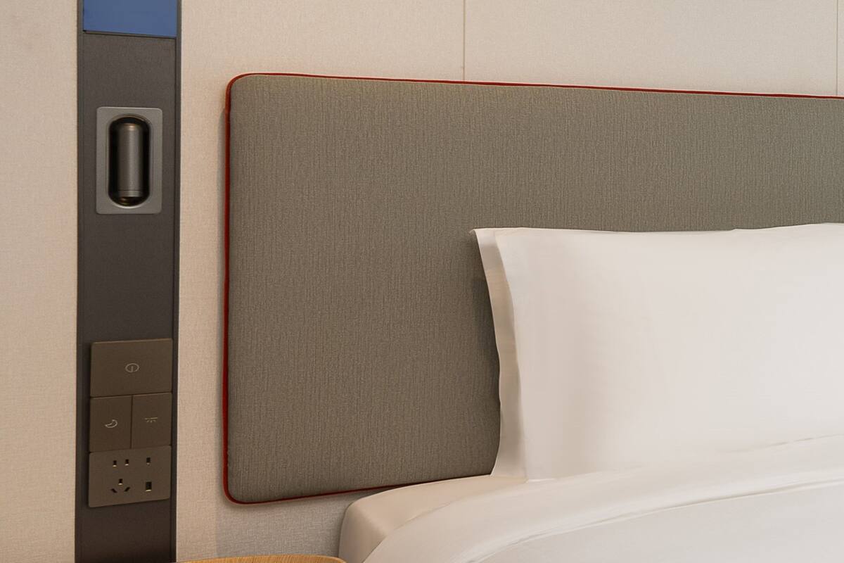 Habitación de hotel con una cama bien tendida, un panel de control en la pared y un cabecero con textura.