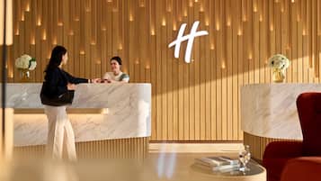 A hotel reception area with wooden paneling, marble reception counters, and a red armchair.