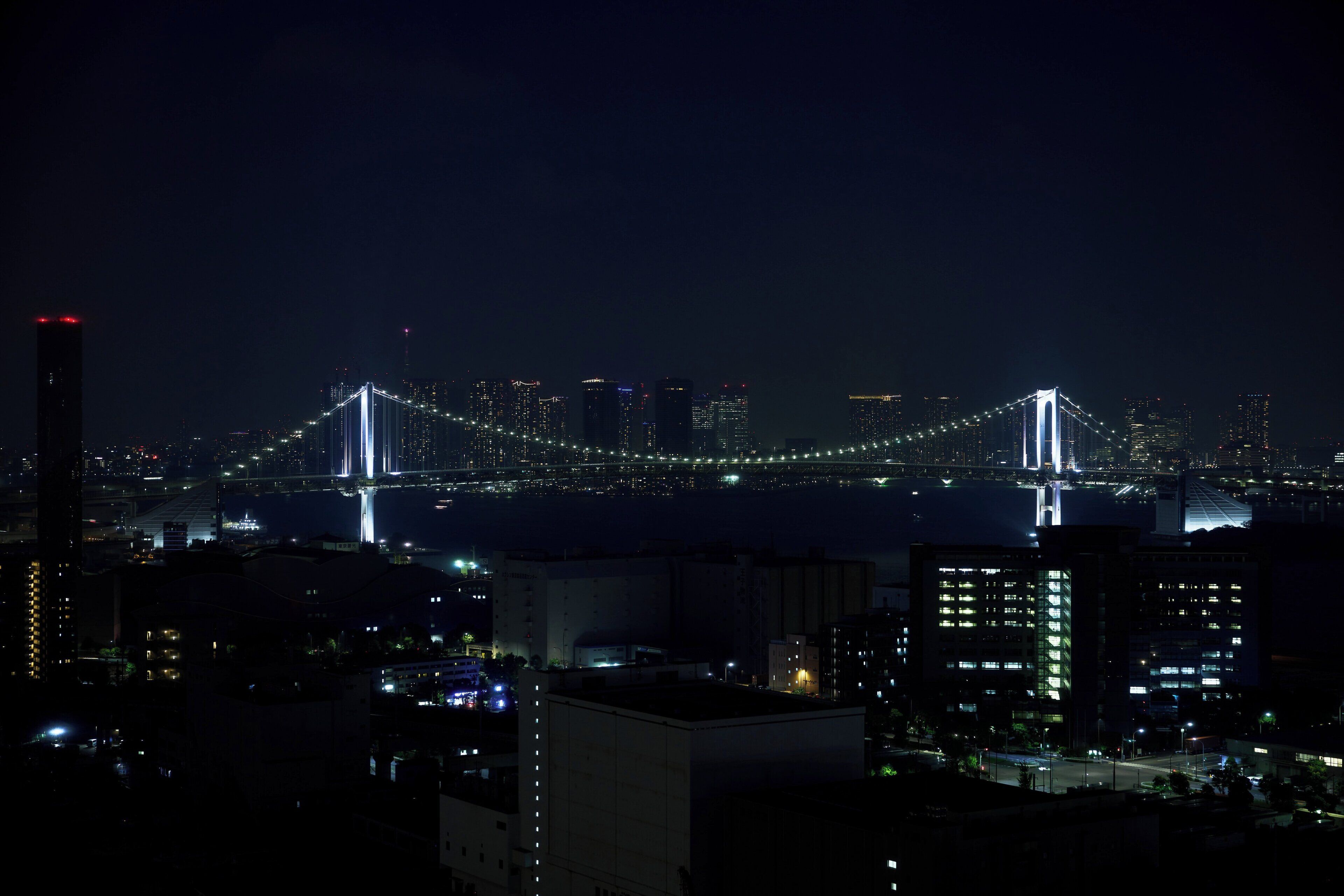 A nighttime cityscape with a prominent illuminated bridge and high-rise buildings.