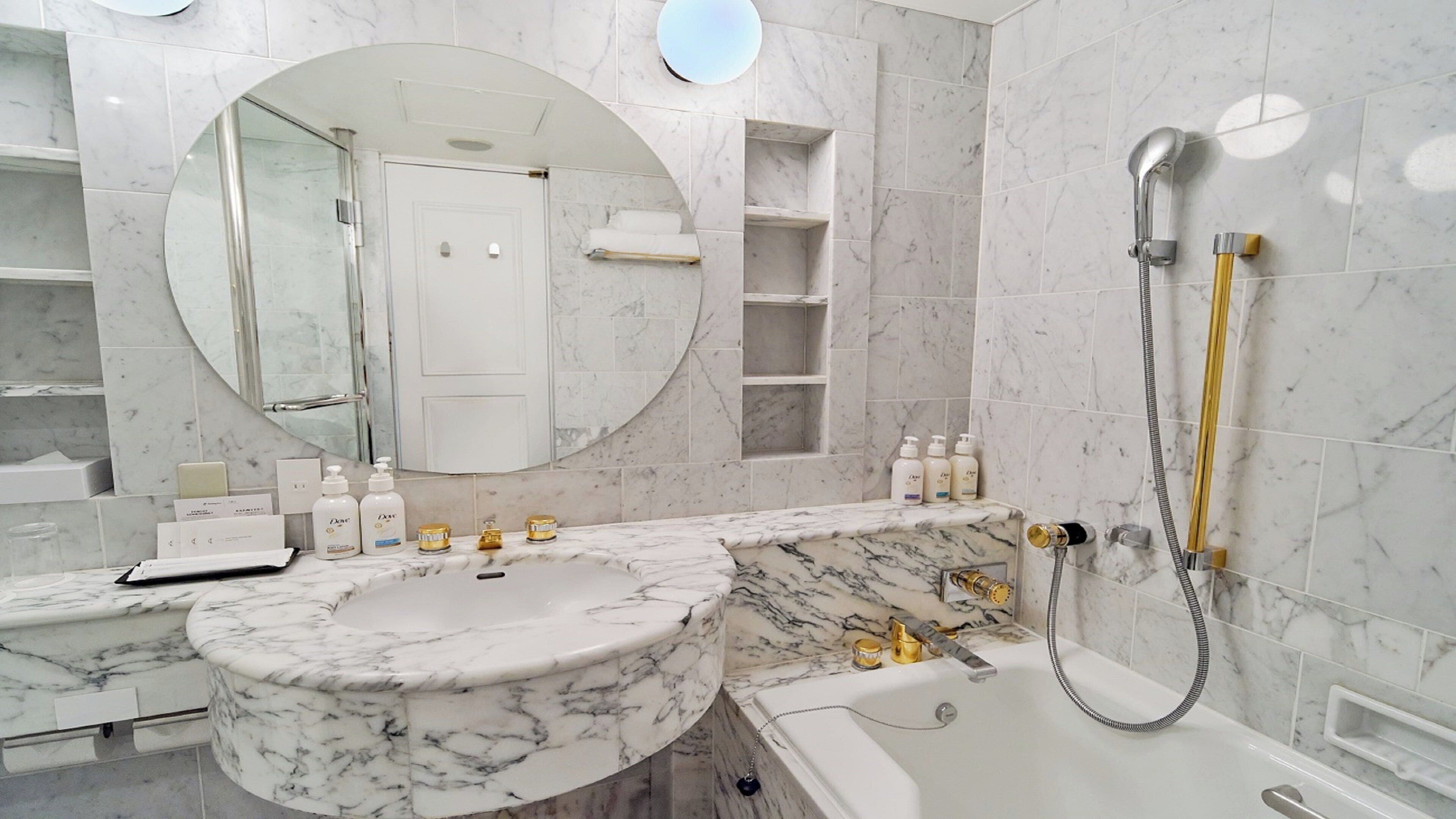 A bathroom with a marble sink, a bathtub, and a shower. There are toiletries on the counter, and a mirror above the sink.