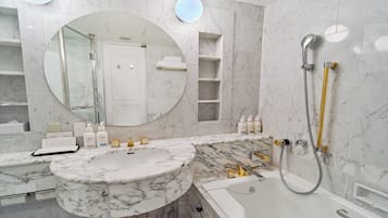 A bathroom with a marble sink, a bathtub, and a shower. There are toiletries on the counter, and a mirror above the sink.