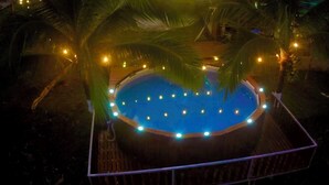 Una vasca idromassaggio circondata da palme e illuminata da luci decorative.