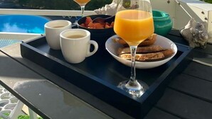 Un vassoio per la colazione con caffè, succo d'arancia e pasticceria su un balcone con vista su una piscina e montagne.