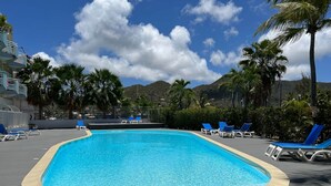 Una piscina rettangolare con un pontile in legno tutt'intorno, dotata di poltrone da relax blu.