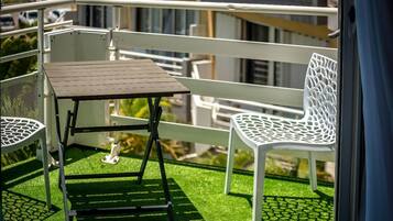 A balcony with a small table and two white chairs on artificial grass.