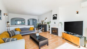 A modern living room with a sofa, coffee table, TV stand, fireplace, and decorative plants. - Casa Londamba | Meia Praia Beach House | Lagos Sea View (Lagos)