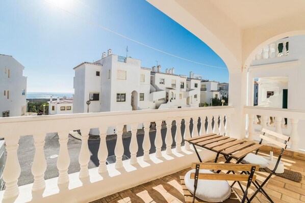 A balcony with white balustrades, wooden furniture, and a view of white buildings and the sea. - Casa Londamba | Meia Praia Beach House | Lagos Sea View (Lagos)
