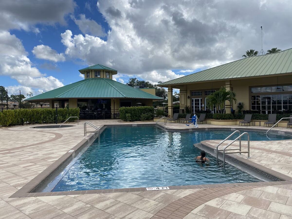 A swimming pool with a 4-foot depth marker, surrounded by a tiled deck and a building with a green roof.