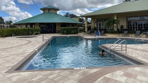 A swimming pool with a 4-foot depth marker, surrounded by a tiled deck and a building with a green roof. - House for long-term rentals in Naples, Florida (Naples)