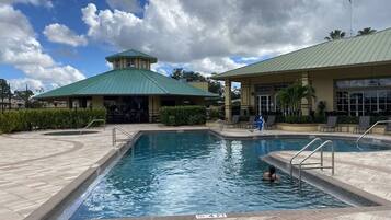 A swimming pool with a 4-foot depth marker, surrounded by a tiled deck and a building with a green roof.