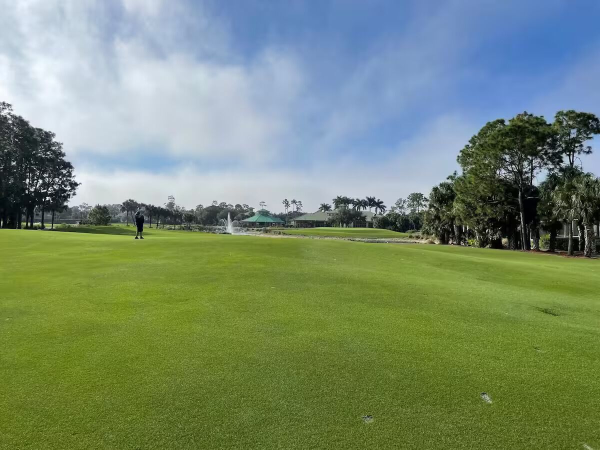 A golf course with a putting green, trees, and a distant building.