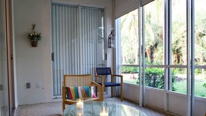 A room with a glass table, two chairs, a wicker sofa, and a view of a garden through large windows. - House for long-term rentals in Naples, Florida (Naples)