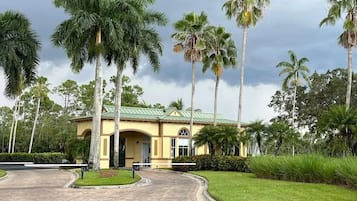 A yellow building with a green roof, surrounded by palm trees and a well-maintained lawn.